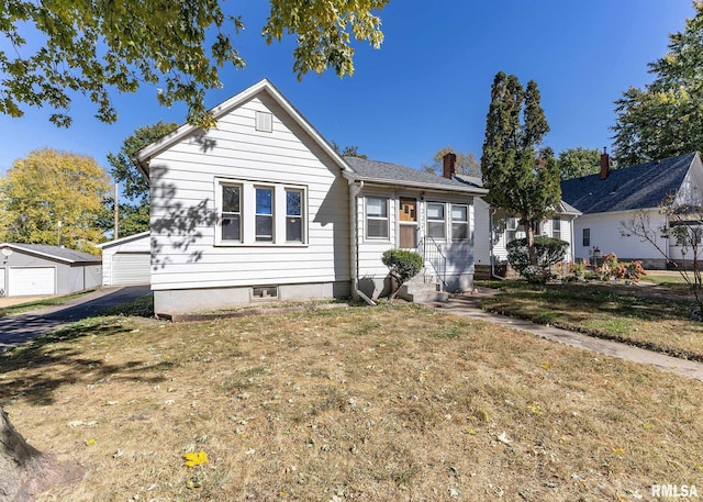 bungalow featuring a front yard, a garage, and an outbuilding