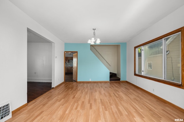 empty room featuring an inviting chandelier and light hardwood / wood-style floors