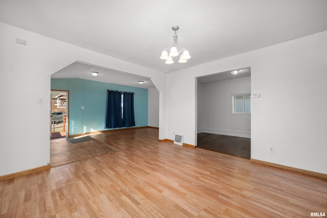 spare room featuring a notable chandelier and light wood-type flooring