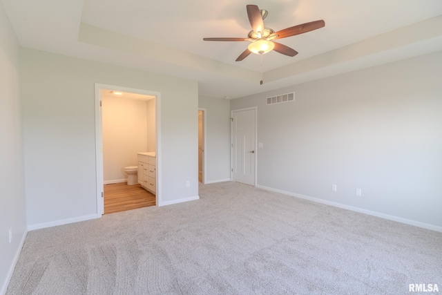 941 9th Ave N, Clinton, IA 52732 - unfurnished bedroom with light colored carpet, connected bathroom, a raised ceiling, and a ceiling fan
