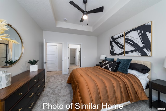 bedroom featuring light carpet, a textured ceiling, a raised ceiling, and ceiling fan