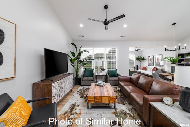 living room with vaulted ceiling, ceiling fan with notable chandelier, and light wood-type flooring