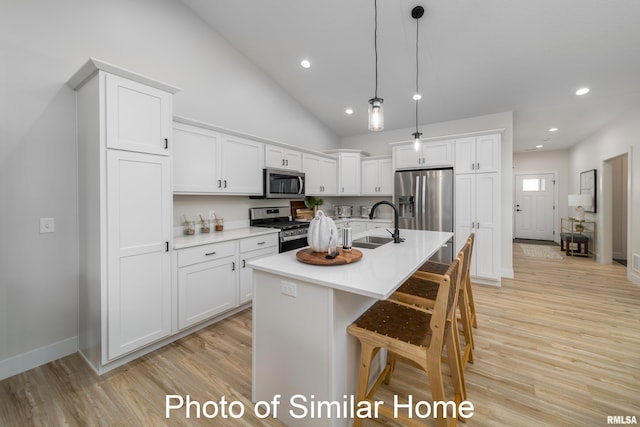 kitchen with white cabinetry, light hardwood / wood-style floors, stainless steel appliances, decorative light fixtures, and a kitchen island with sink