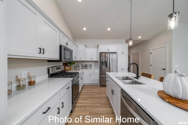 kitchen with appliances with stainless steel finishes, white cabinetry, light wood-type flooring, sink, and decorative light fixtures