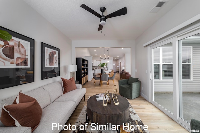 living room with a textured ceiling, light hardwood / wood-style flooring, and ceiling fan with notable chandelier