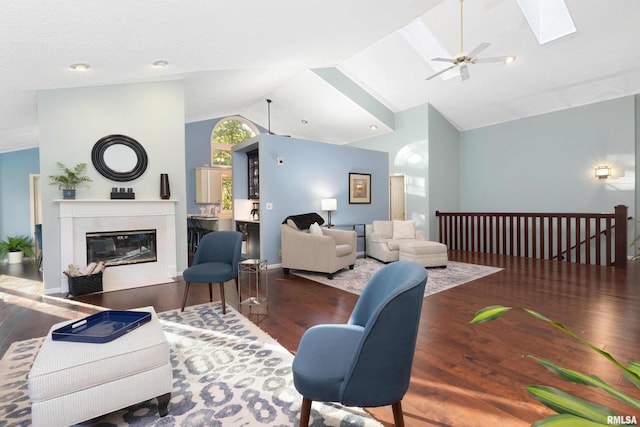 living room with dark wood-type flooring, high vaulted ceiling, a skylight, and ceiling fan