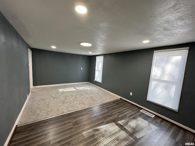spare room featuring a textured ceiling, visible vents, baseboards, recessed lighting, and wood finished floors
