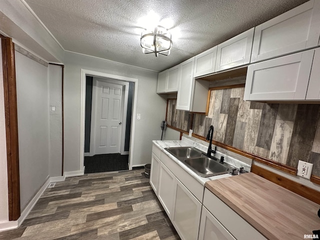 kitchen with white cabinets, a textured ceiling, a sink, butcher block counters, and dark wood-type flooring