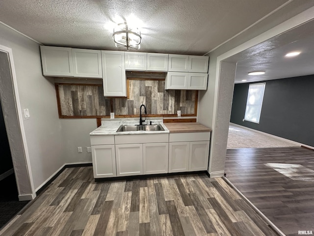 kitchen with a sink, a textured ceiling, decorative backsplash, white cabinets, and dark wood-style flooring