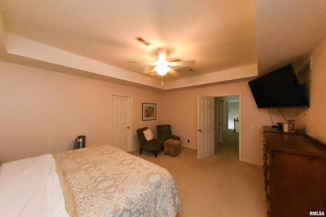 bedroom with light carpet, a tray ceiling, and ceiling fan