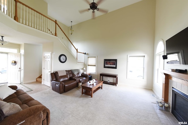 carpeted living room with ceiling fan, a towering ceiling, and a tile fireplace