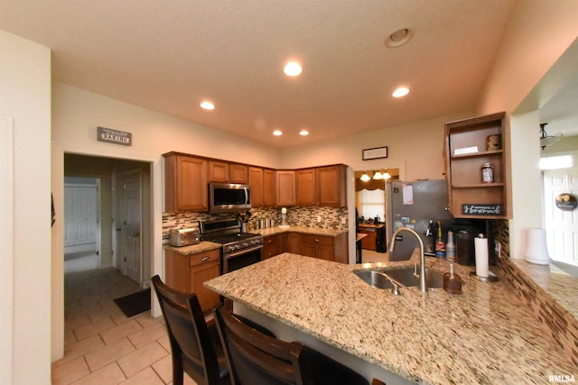 kitchen featuring kitchen peninsula, appliances with stainless steel finishes, a breakfast bar, light stone countertops, and sink