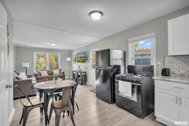 kitchen with white cabinets, backsplash, light stone countertops, light wood-type flooring, and black appliances