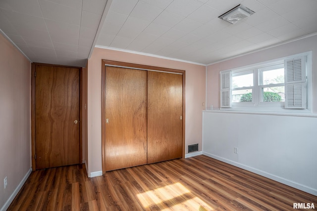 unfurnished bedroom featuring crown molding, a closet, and dark wood-type flooring