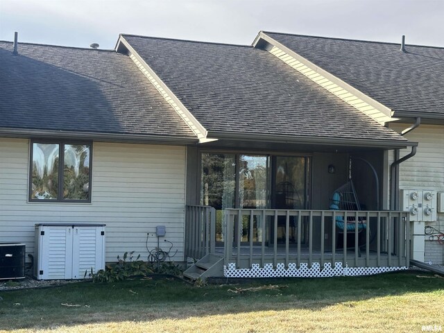 rear view of house featuring a wooden deck, a yard, central air condition unit, and roof with shingles