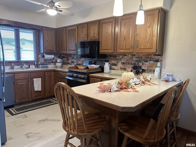 kitchen featuring stainless steel range with gas cooktop, a peninsula, a sink, black microwave, and light countertops