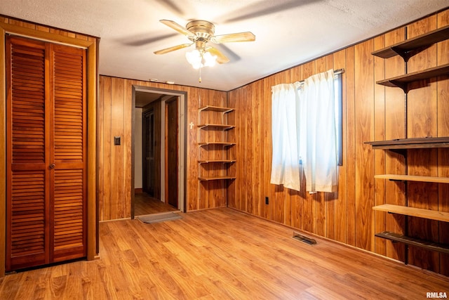 unfurnished bedroom featuring light hardwood / wood-style flooring, ceiling fan, and wooden walls