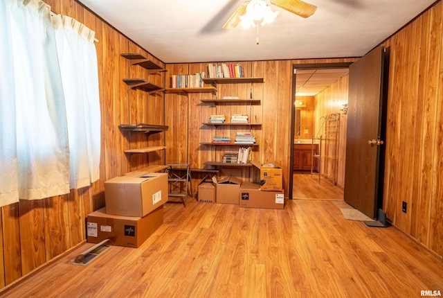 interior space with wood walls, ceiling fan, and light wood-type flooring