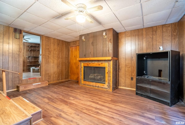 unfurnished living room with wooden walls, a drop ceiling, ceiling fan, and hardwood / wood-style flooring