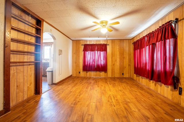 empty room with built in shelves, ceiling fan, ornamental molding, and wood-type flooring