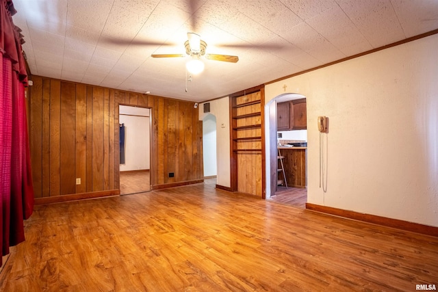 unfurnished room with ceiling fan, light wood-type flooring, crown molding, and built in shelves