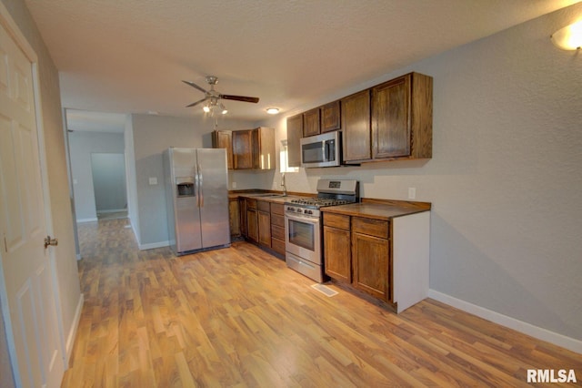 kitchen featuring a textured ceiling, stainless steel appliances, ceiling fan, sink, and light hardwood / wood-style flooring