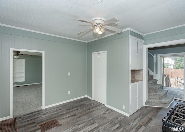 unfurnished room with wood walls, ornamental molding, dark wood-type flooring, and ceiling fan