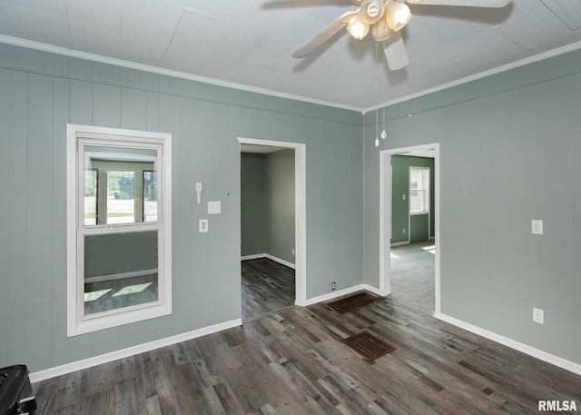 empty room with wood walls, ornamental molding, dark wood-type flooring, and ceiling fan