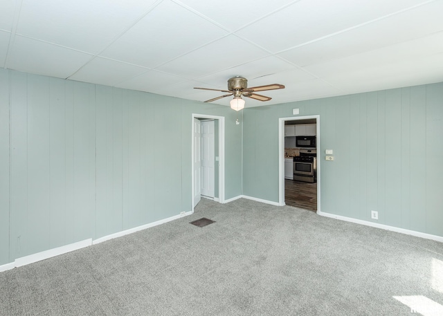 empty room featuring ceiling fan, wood walls, and carpet floors