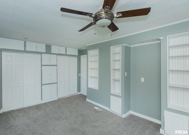 unfurnished bedroom featuring multiple closets, crown molding, light colored carpet, and ceiling fan