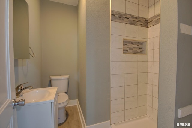 bathroom featuring vanity, tiled shower, wood-type flooring, and toilet