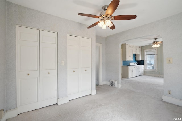 unfurnished bedroom with ceiling fan, light colored carpet, and multiple closets