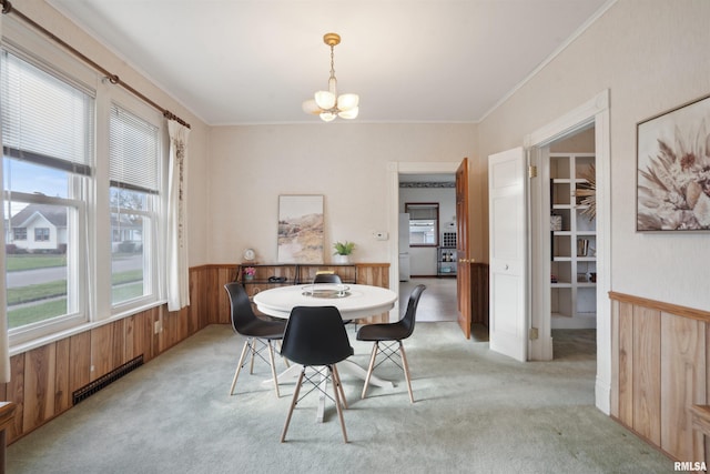 carpeted dining room with an inviting chandelier, ornamental molding, and wood walls