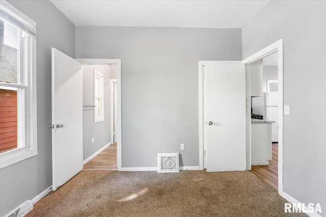 unfurnished bedroom with light hardwood / wood-style flooring, multiple windows, white fridge, and a closet