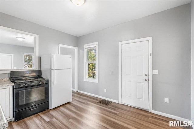 kitchen with light hardwood / wood-style flooring, white cabinetry, black gas range oven, and white refrigerator