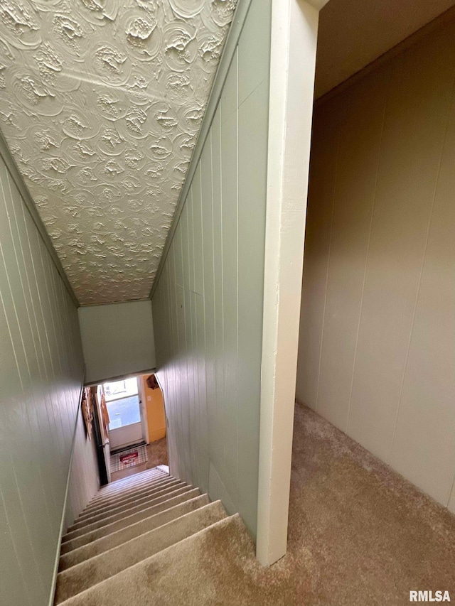 stairs featuring carpet, vaulted ceiling, a textured ceiling, and wood walls