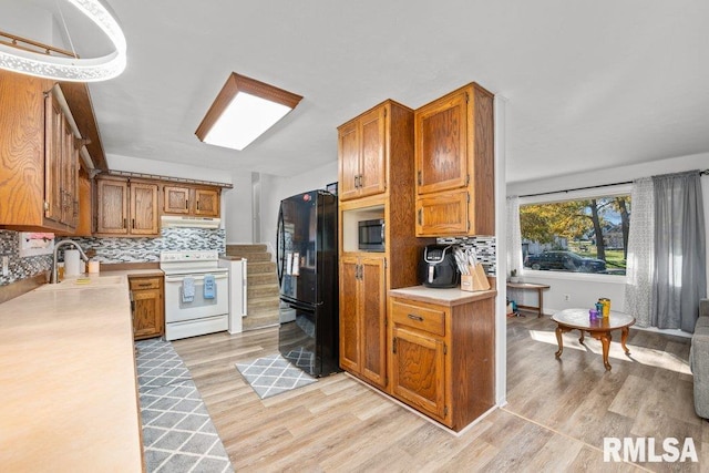 kitchen featuring tasteful backsplash, sink, light wood-type flooring, black fridge, and white electric range