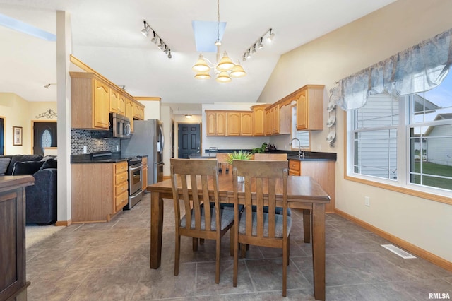 kitchen featuring stainless steel appliances, track lighting, tasteful backsplash, lofted ceiling, and a notable chandelier