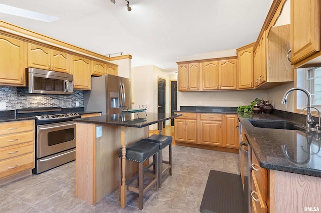 kitchen with sink, appliances with stainless steel finishes, dark stone counters, a breakfast bar area, and a kitchen island