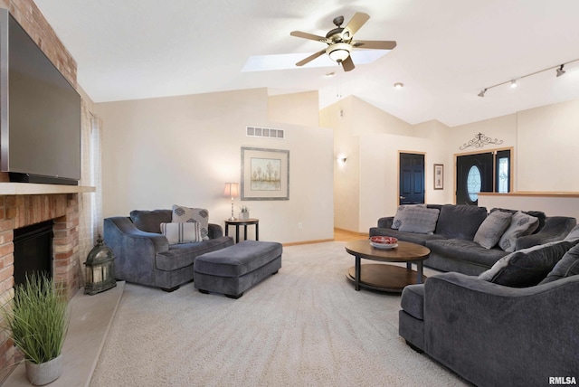 living room with ceiling fan, rail lighting, a fireplace, lofted ceiling, and light colored carpet