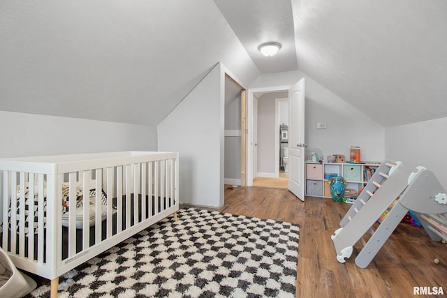 bedroom with vaulted ceiling, hardwood / wood-style flooring, and a nursery area