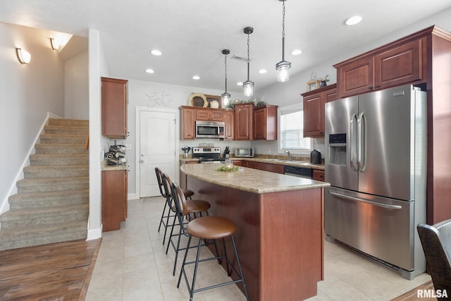 kitchen with appliances with stainless steel finishes, a kitchen bar, a center island, light hardwood / wood-style floors, and pendant lighting