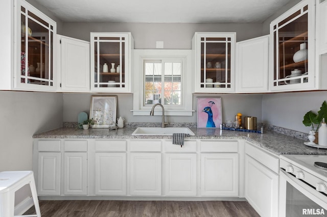 kitchen with white cabinets, sink, light stone countertops, dark hardwood / wood-style flooring, and range