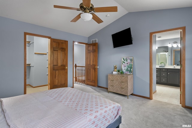 bedroom featuring lofted ceiling, ensuite bathroom, a walk in closet, ceiling fan, and light colored carpet