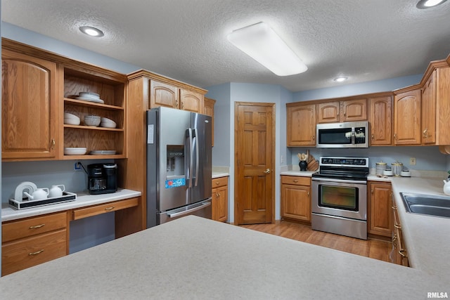 kitchen with appliances with stainless steel finishes, a textured ceiling, light hardwood / wood-style flooring, and sink