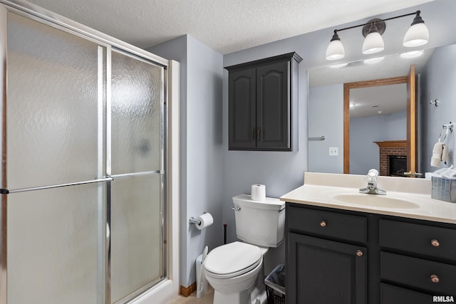 bathroom with a textured ceiling, vanity, a shower with door, a fireplace, and toilet