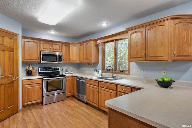 kitchen with appliances with stainless steel finishes, a textured ceiling, light hardwood / wood-style flooring, and sink