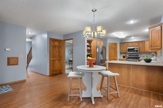 kitchen with a breakfast bar, light wood-type flooring, a notable chandelier, kitchen peninsula, and stainless steel appliances