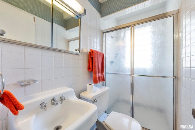 bathroom featuring toilet, sink, a shower with shower door, and tile walls