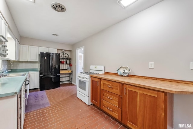 kitchen with butcher block counters, gas range gas stove, sink, black fridge, and white cabinets